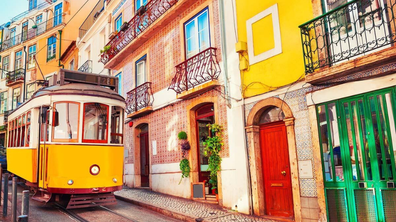 Classic yellow tram rolling through a cool neighborhood in Lisbon, surrounded by colorful tiled buildings and old-world charm.