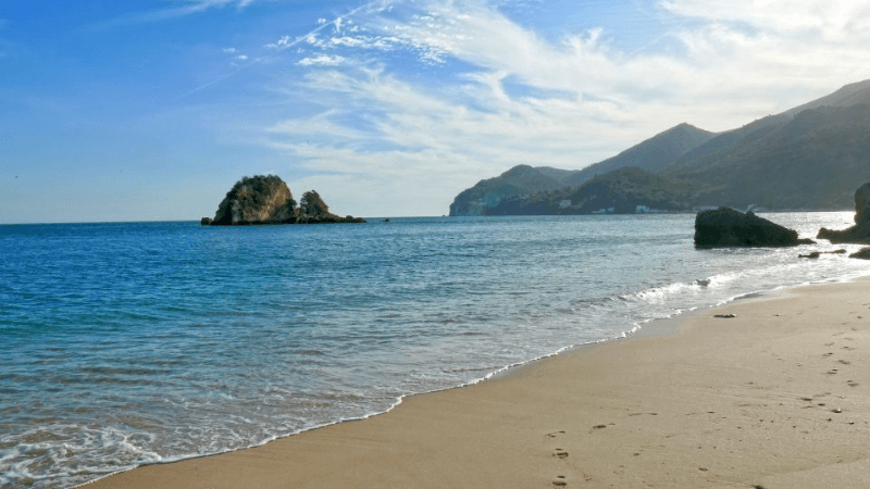 Soft sandy shore and shallow waters at Praia da Figueirinha, one of the best beaches near Lisbon Portugal